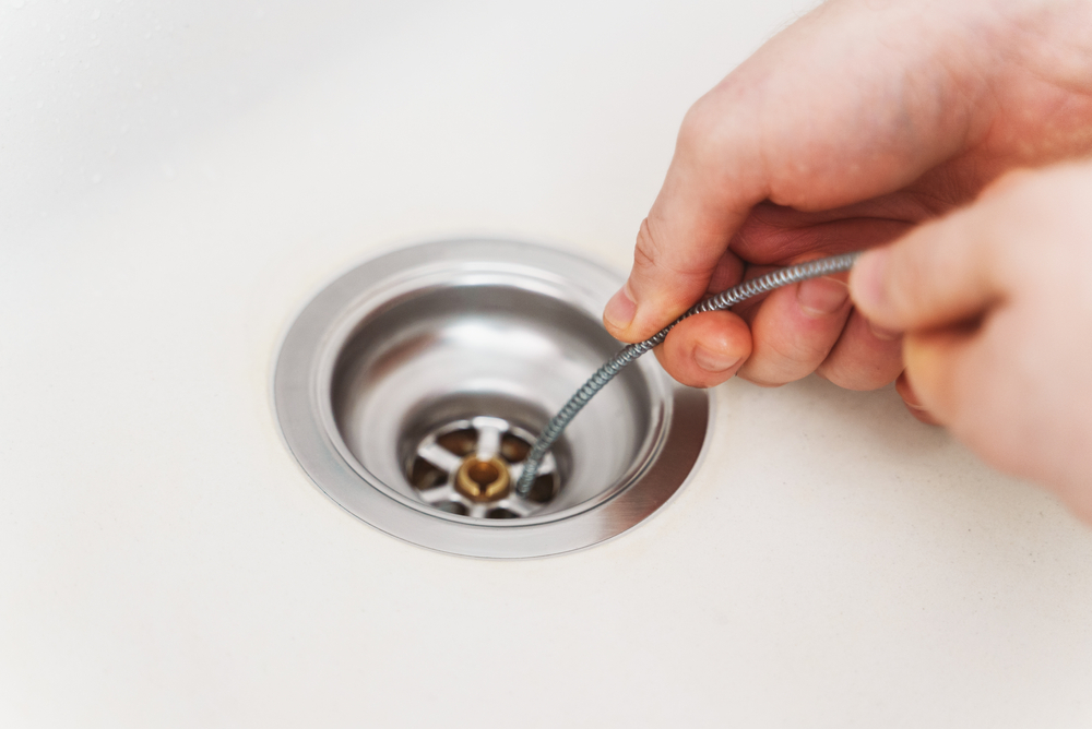 a professional plumber's hands holding onto a drain snake that's inserted into a kitchen sink