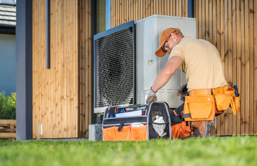 An HVAC technician kneeling beside an outdoor unit while performing maintenance